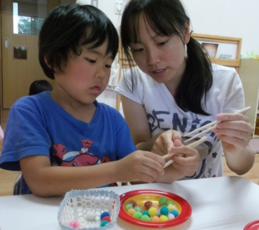 保育士に箸の持ち方を教わっている写真